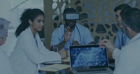 Collaborating medical team in scrubs and white coats in training room, using VR headset and laptop