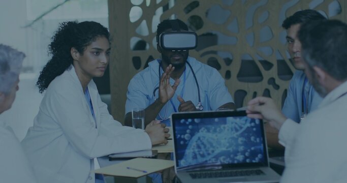 Collaborating medical team in scrubs and white coats in training room, using VR headset and laptop