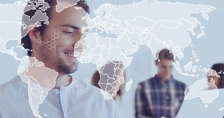 Smiling adult man wearing light collared shirt standing in bright office, showing map with hex UI
