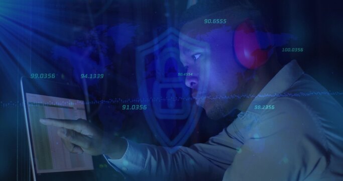 Pointing man in shirt, red headset leaning toward laptop at control desk, with shield and overlays