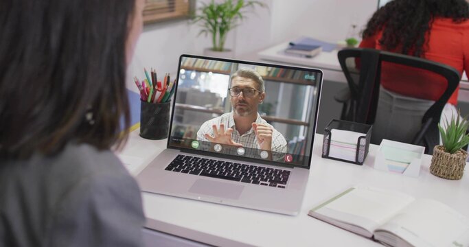 Watching woman in grey blazer joining call on laptop at office, coworker in red top working