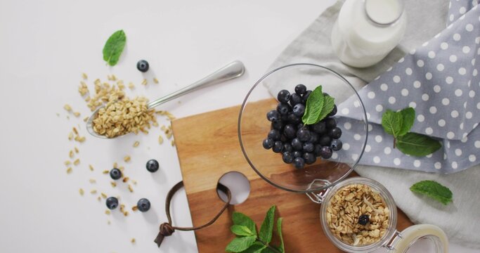 Fototapeta Displaying glass bowl of blueberries with mint sprig on wooden cutting board, with granola
