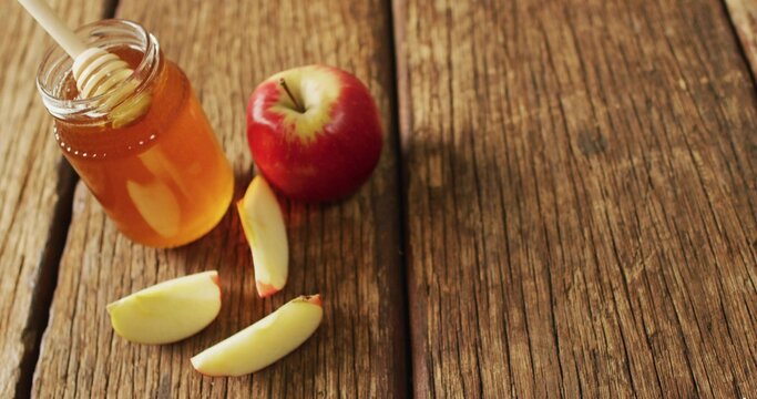 Displaying honey jar with wooden dipper, red apple and three slices on rustic table, copy space