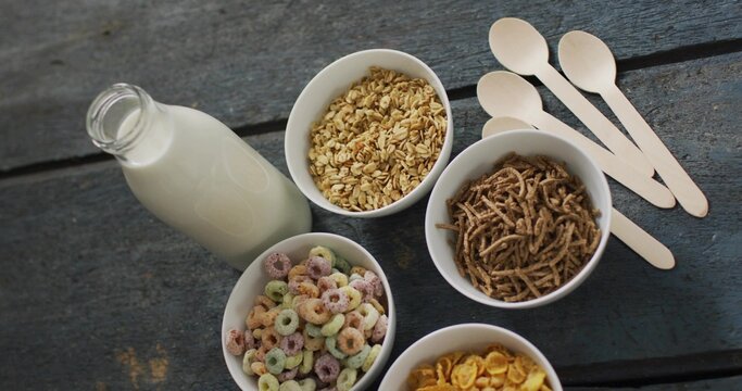 Showcasing five white bowls holding cereals on dark wooden table, with milk bottle and spoons