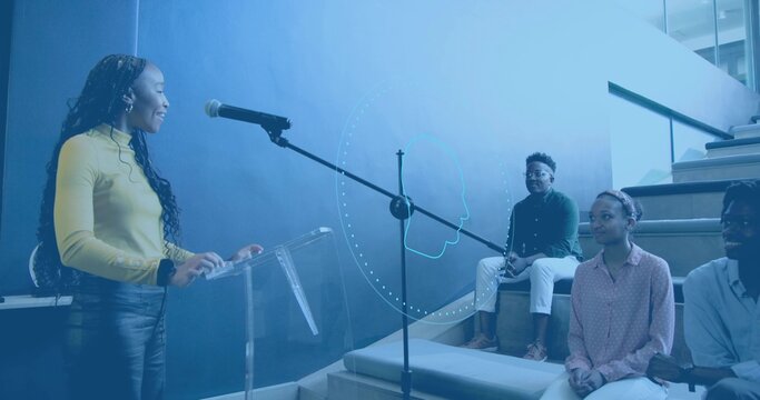 Speaking woman wearing mustard yellow top and dark pants at clear lectern with mic, copy space