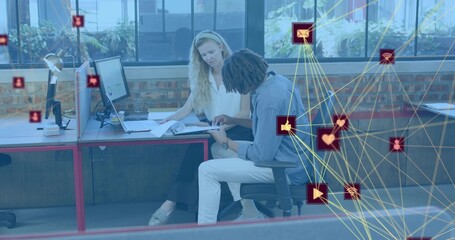Reviewing two colleagues leaning forward pointing at documents on desk in office, network overlay