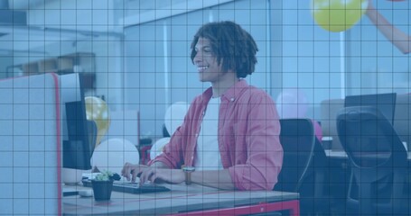 Typing younger adult male wearing pink shirt at open-plan office, with succulent and balloons