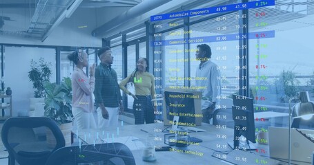 Analyzing team in business reviewing stock tickers on glass wall at office with laptops and mugs