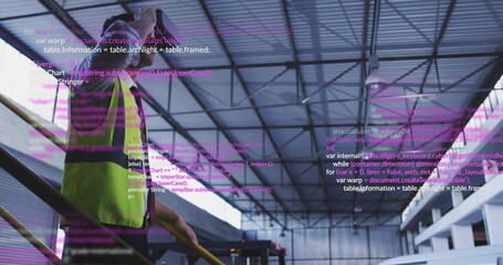 Standing man wearing hi-vis vest shading eyes on handrail in plant, holding yellow pole, copy space