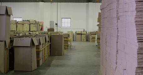 Filling right side tall stack flat cardboard sheets in warehouse aisle, with pallets, copy space