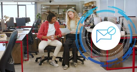 Reviewing printed sheet, two coworkers wearing red shirt and yellow knit at office, envelope icon