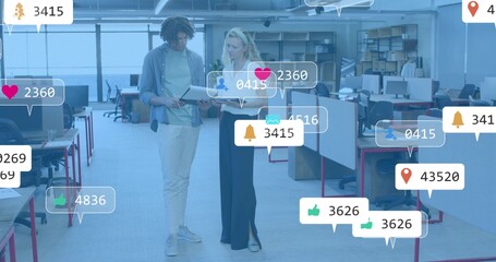 Reviewing tablet, two coworkers in casual wear pointing and discussing in open office with alerts
