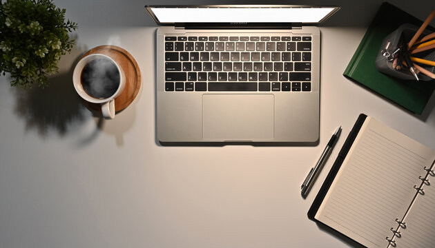 Top view of laptop, coffee cup, laptop, pen, and potted plant on white desk