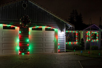 Garage doors are decorated with Christmas garlands, red ribbons, balls and a wreath at night