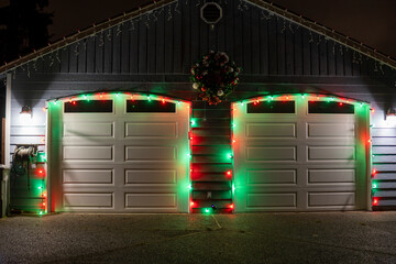 Garage doors are decorated with Christmas garlands, red ribbons, balls and a wreath at night