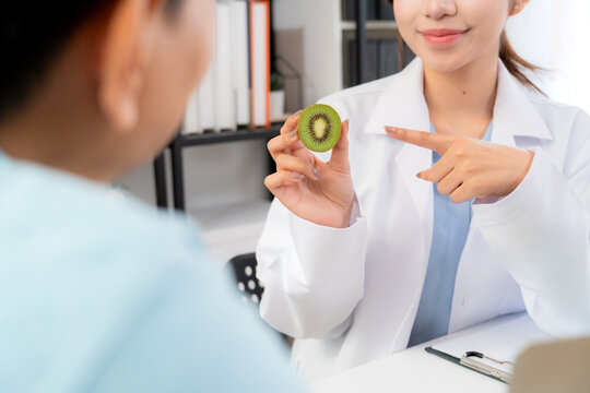 Close up asian nutritionist holding kiwi fruit to advise and consultation male patient in clinic, healthcare discussion and healthy food, doctor guidance nutrition with man, meal plan planning.