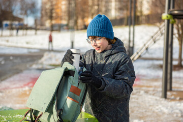 A child in a blue knit beanie and warm winter coat reaches into a mint-green backpack to take a...