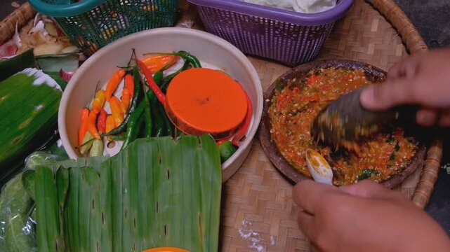 A traditional Indonesian sambal terasi being made with a stone mortar and pestle, featuring freshly ground chilies, tomatoes, and shrimp