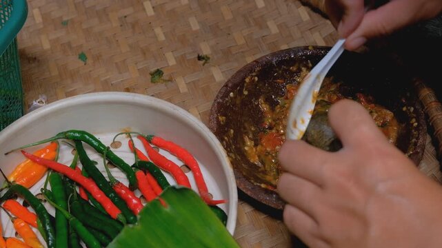 A traditional Indonesian sambal terasi being made with a stone mortar and pestle, featuring freshly ground chilies, tomatoes, and shrimp