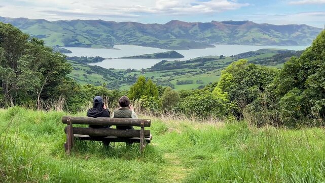 Couple enjoys scenic view of Akaroa Peninsula from bench in New Zealand