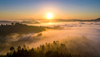 Aerial view of a radiant sunrise over forested hills partially obscured by a thick blanket of fog. The bright sun is centered in the frame