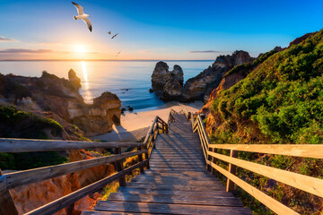 Wooden Stairs Leading Down to a Secluded Beach Cove at Sunset, Coastal Cliffs, Ocean View, and Seagulls Flying in Algarve, Portugal