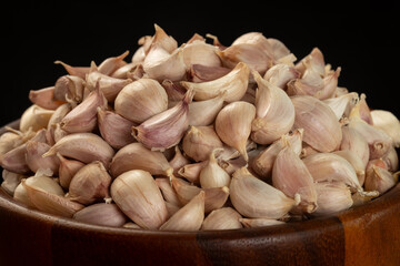 Pile of Thai garlic cloves in a brown wooden bowl on a black background. Close-up