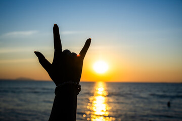 silhouetted hand making the "I Love You" sign in front of a radiant sunset over the ocean