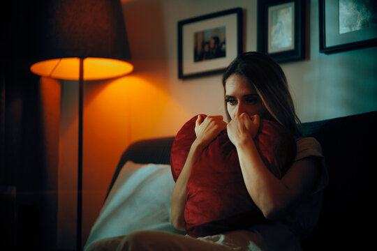 Sad Woman Holding a Heart Shaped Pillow Being Depressed. Unhappy stressed girlfriend suffering after a painful break up 
