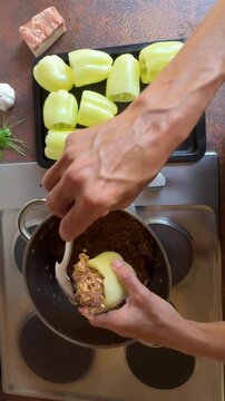 directly above shot chef preparing food in kitchen, making stuffed capsicum, filling yellow paprika shells with minced meat