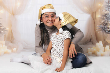 Divorced single mother and her 5-year-old Latina daughter with glasses excited celebrate Christmas and New Year's together, wearing Santa hats