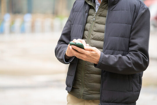 Senior man's hands holding green smartphone, typing message outdoors
