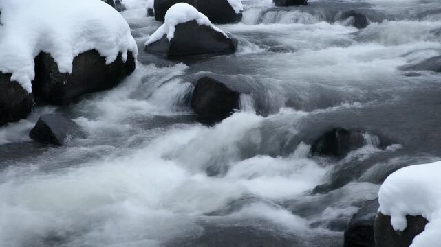 Fast Flowing Icy River Through Snow Covered Boulders.