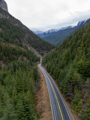 Winding Mountain Road Through Dense Pine Forest In BC, Canada, Meandering Toward Snow-Capped Peaks