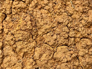 Abstract close-up texture of dry, cracked, clumpy brown soil. Macro shot of earth surface showing drought or poor structure.
