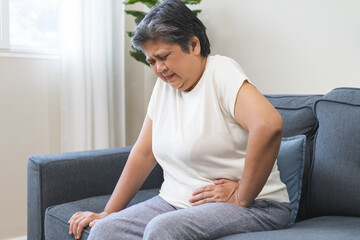 Sick asian senior woman in pain, hand holding belly, stomach pain from food poisoning, older hurt...