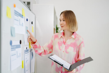Business woman reviewing data and planning strategy on a whiteboard in a bright modern office.
