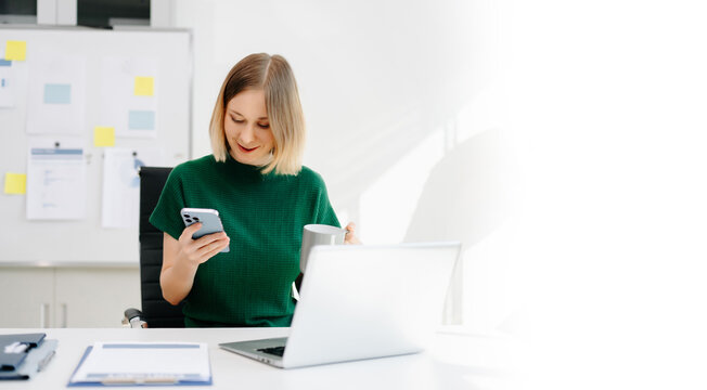 Business woman reviewing documents while checking her smartphone at a bright modern desk.