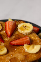 French toast breakfast with sliced strawberries and bananas on a plate topped with syrup – sweet homemade brunch food.