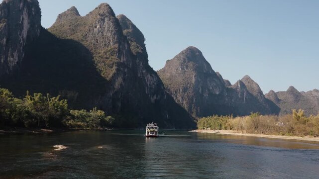 A river cruise boat moves calmly beneath dramatic karst cliffs rising above the Li River in China