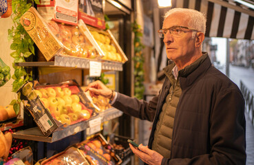 Senior man buying fresh apples at a street market, holding a mobile phone