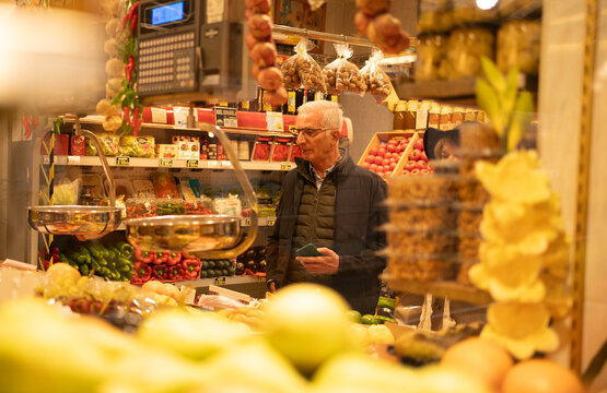Senior man with glasses holding a smartphone while shopping for fresh produce in a grocery store