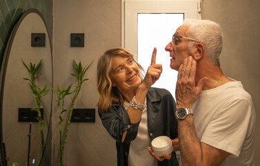 Happy senior couple bonding while applying anti-aging face cream in the bathroom