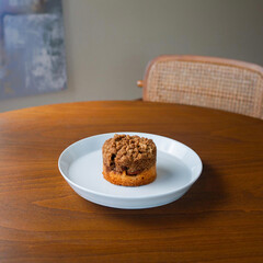 Delicious coffee cake muffin with crumbly streusel topping on a white plate. Freshly baked cinnamon pastry served on a wooden table