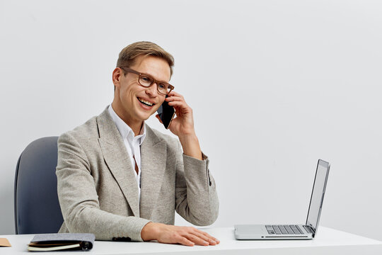 Smiling young caucasian man talking phone sitting at desk with laptop work digital nomad web3 remote office concept