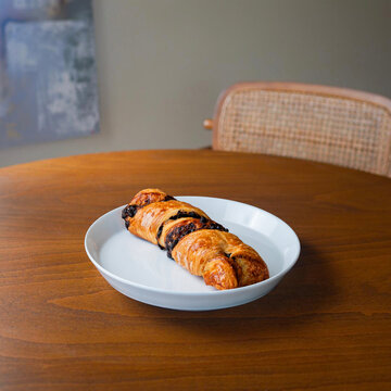 Golden chocolate twist pastry (Torsade) on a white plate. Fresh puff pastry with chocolate chips served on a wooden table
