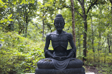 Serene fasting Buddha statue in deep meditation. This spiritual asceticism sculpture sits peacefully in lush green nature forest, symbol of enlightenment and tranquility
