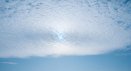 Serene blue sky filled with soft altocumulus clouds illuminated by the sun
