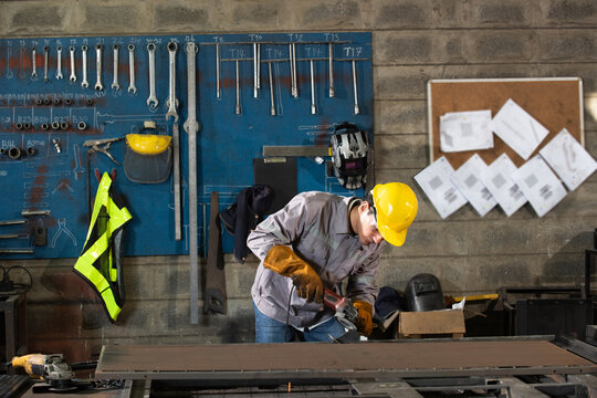 Factory welder in protective gear cuts metal as skilled worker focuses on steel project inside industrial workshop, sparks flying, gritty atmosphere, strong light and shadow, determined mood