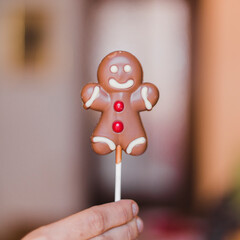 A sweet gingerbread man lollipop held by a hand with a blurred festive background